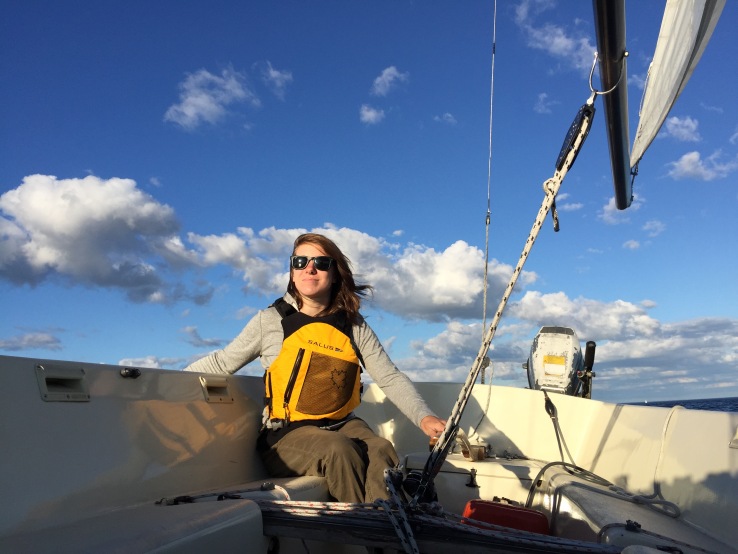 Jessica driving a sail boat while wearing a yellow.